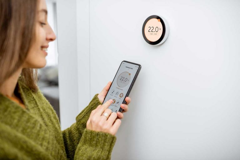 Woman-Regulating-Heating-Temperature-With-Phone-Best-Smart-Thermostats-For-Heat-Pumps
